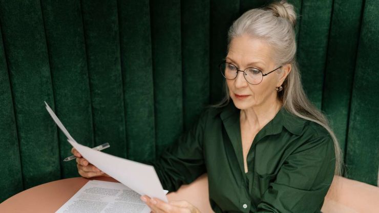 Женщина пенсионного возраста в зеленной блузке читает документы пенсионная системы Казахстана