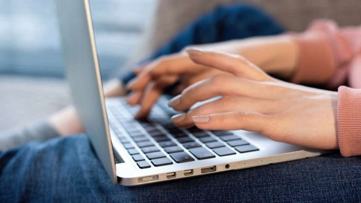 Девушка сидит с ноутбуком на ногах и ищет в интернете варианты выгодных мини кредитов онлайн