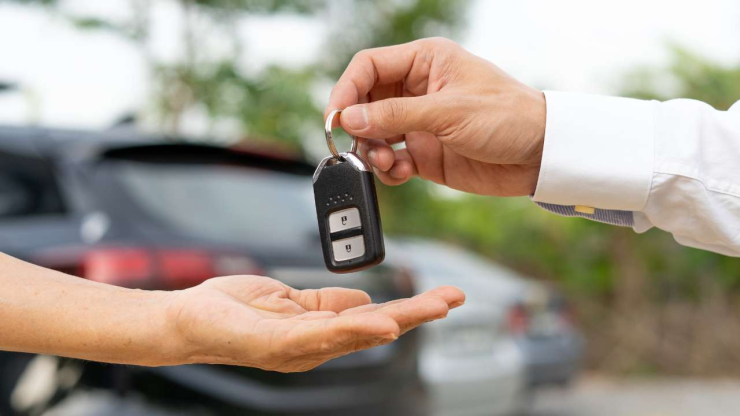 Ключи от автомобиля передаются из рук в руки на фоне машины в кредит без первоначального взноса