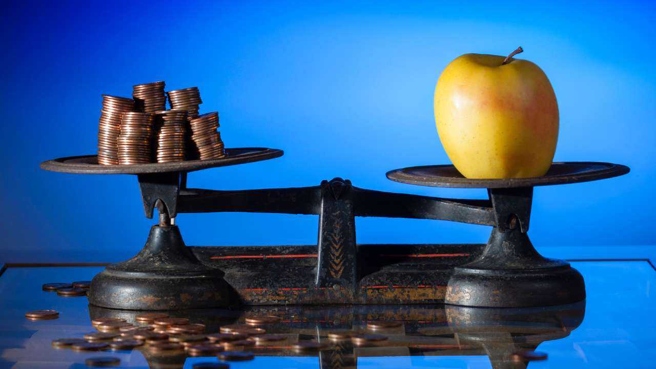 Железные весы уравновешены с одной стороны яблоком и с другой кучей монет – влияние инфляции на личные финансы