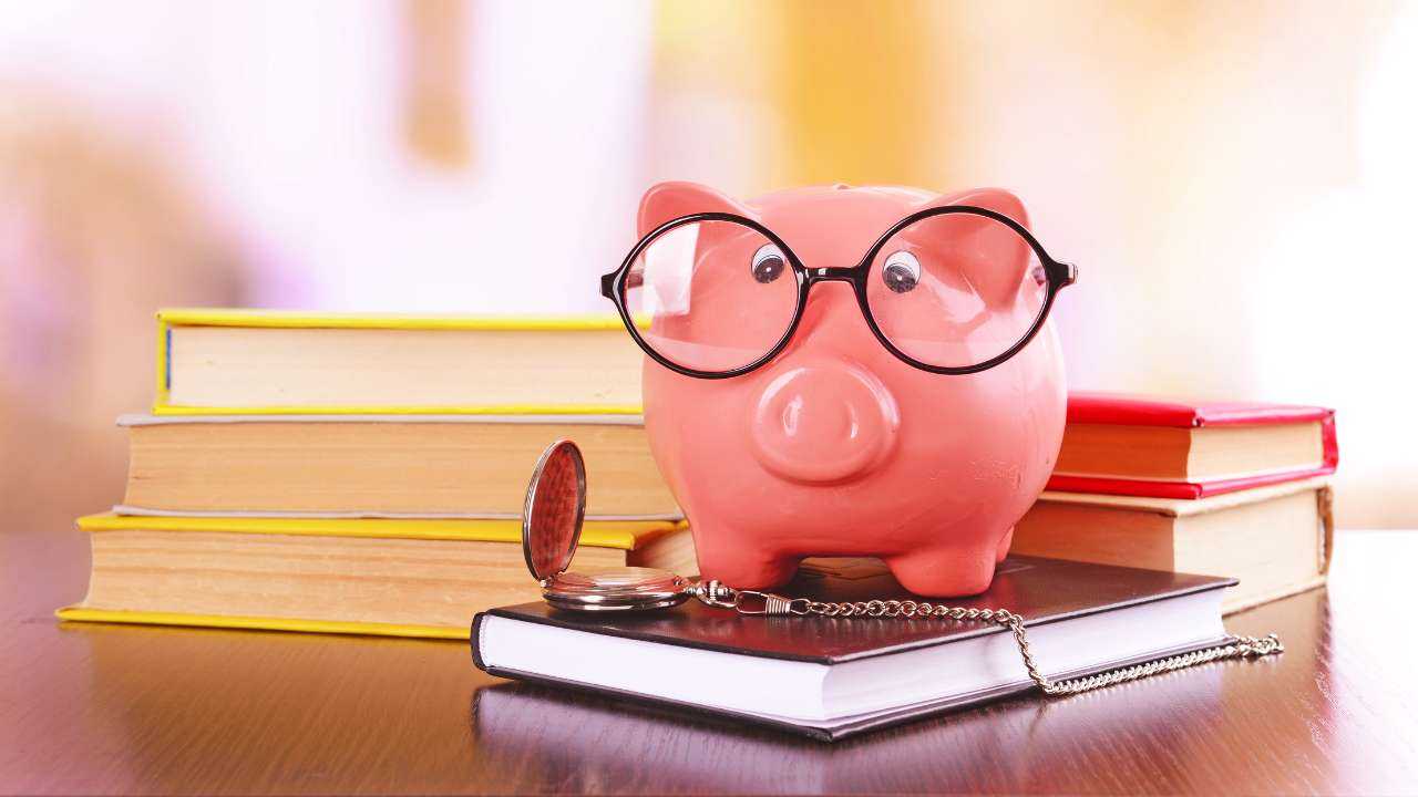 На столе расположены стопки книг, свинка-копилка в очках и часы – время научить детей финансовой грамотности