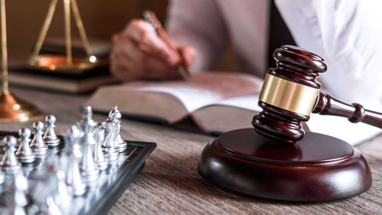 Судья пишет в тетради про наследование кредитов рядом с шахматной доской и молотком на столе