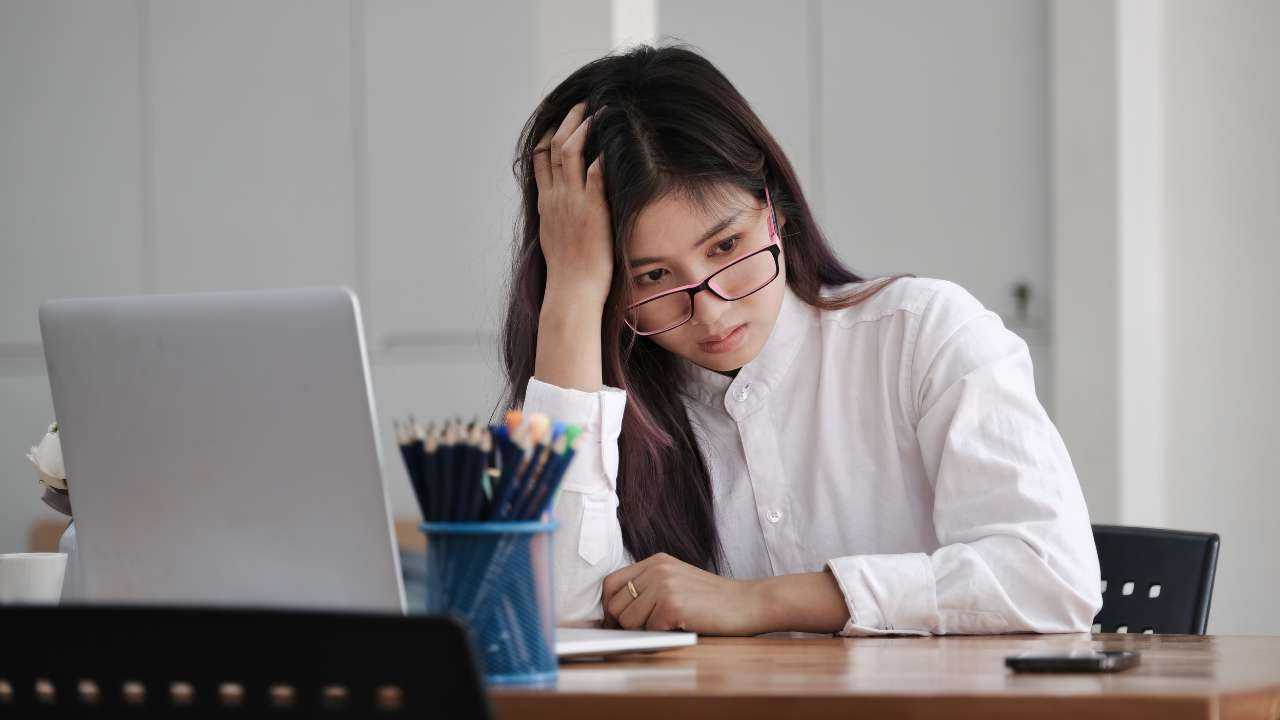 За письменным столом, схватившись за голову, сидит девушка и думает, как лучше подготовиться к финансовому кризису