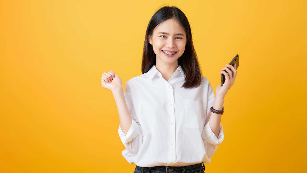 На желтом фоне стоит девушка с телефоном в пуках и широко улыбается, потому что оформила микрокредит с 18 лет