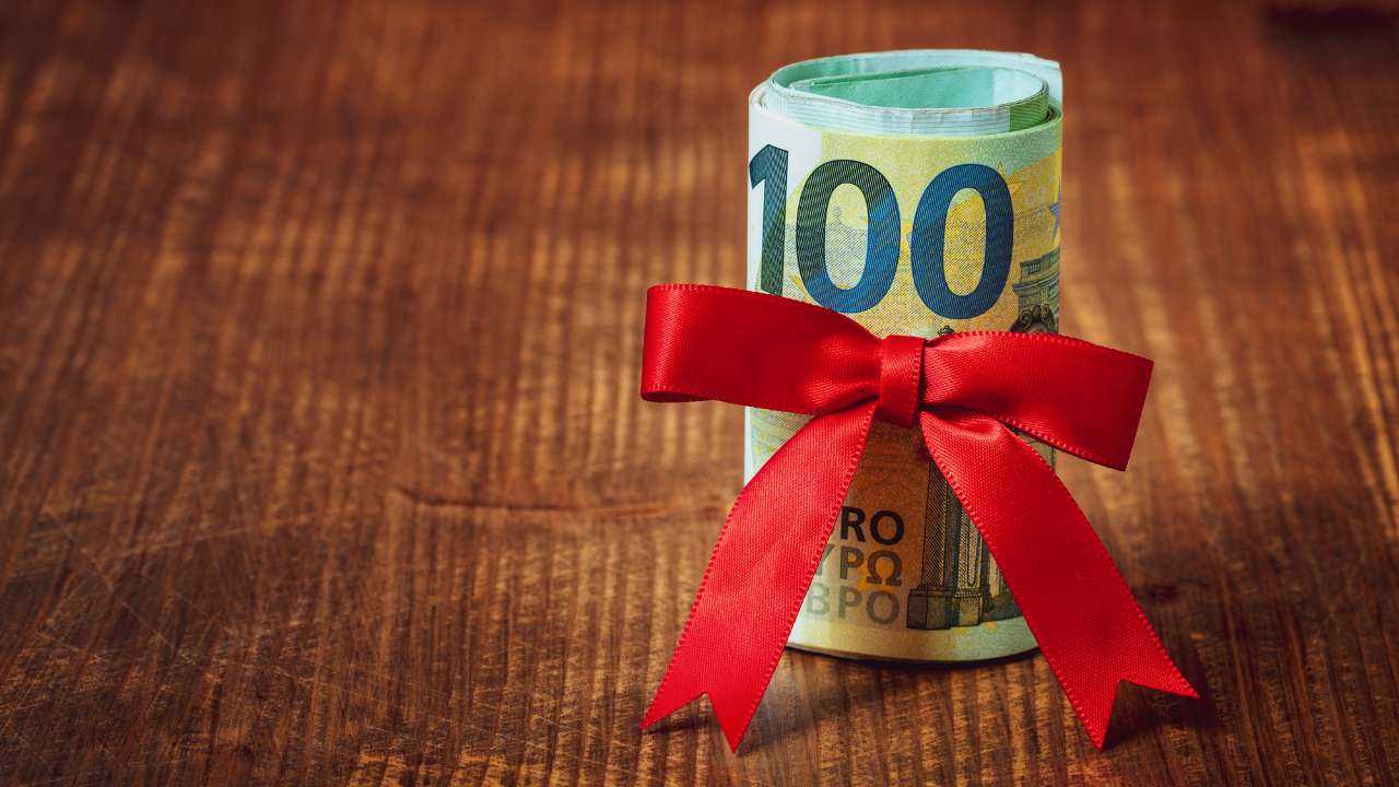 На деревяном столе рулон купюр в 100 евро, обтянутых красной лентой, как идея денежного подарка