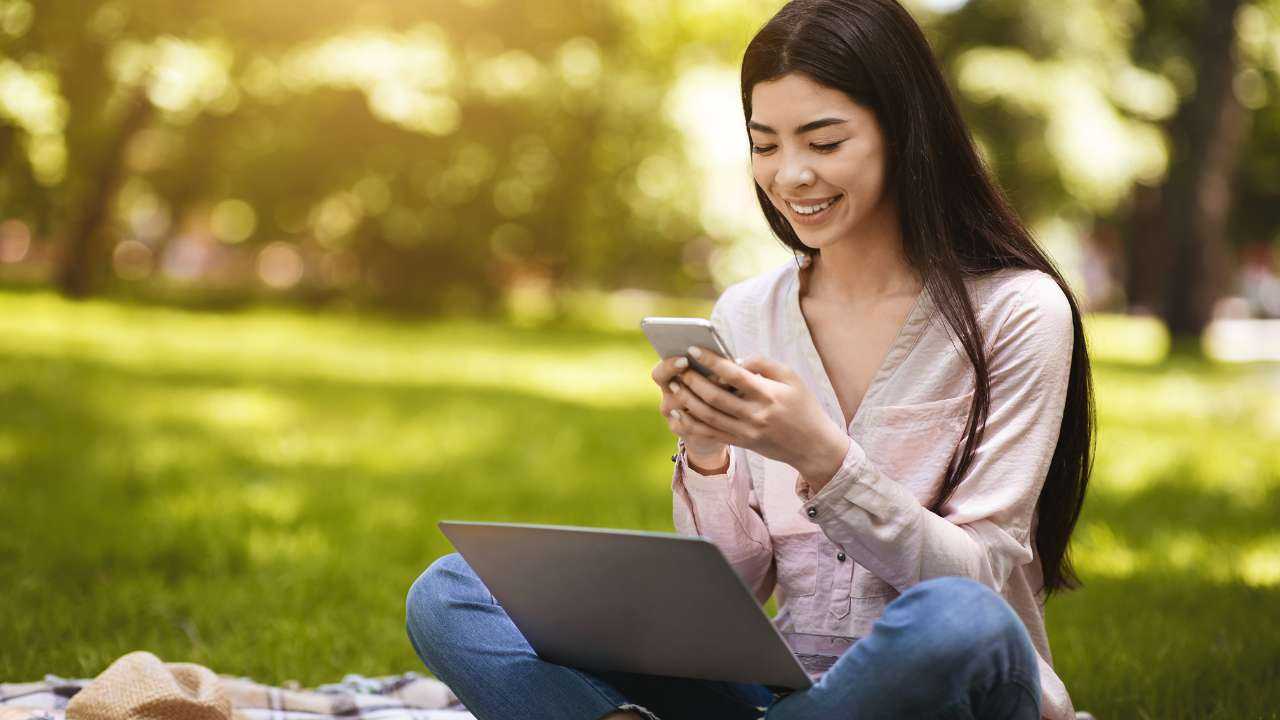 Девушка сидит в парке и в смартфоне использует финансовое приложение для интерактивного обучения финансовой грамотности